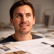 Diseñador de producto independiente en estudio creativo, con muestras de material y plano sobre la mesa